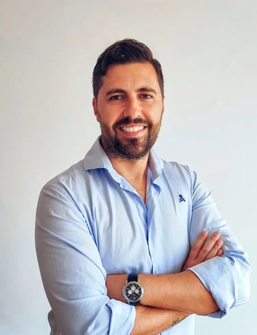 A smiling professional businessman in a light blue button-down shirt with crossed arms.