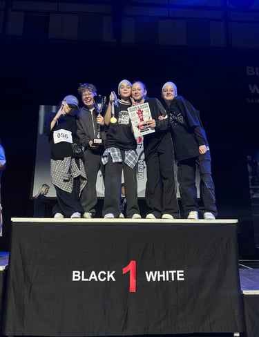 Young hip hop dance crew celebrating on stage with a first place trophy and gold medal.