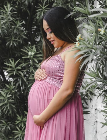 a pregnant woman wearing a pink dress in front of some tropical plants