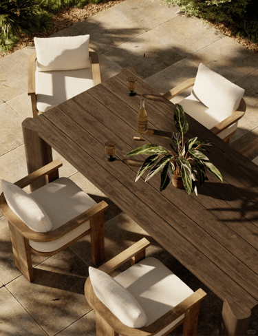 Outdoor wooden table with cushioned chairs, plant centerpiece and natural stone flooring, creating a