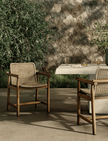 Garden seating area with woven armchairs, small outdoor table, stone wall and natural greenery for a