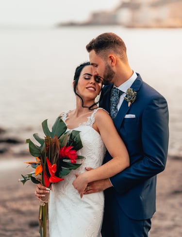 una novia y un novio en una playa abrazándose en el día de su boda