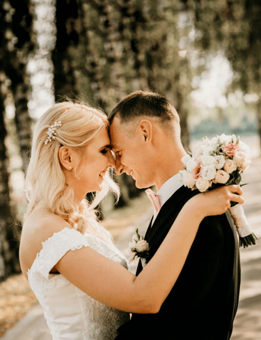 a bride and groom standing in front of a tree. Vestuvės, jaunikis ir jaunoji žiūri vienas į kitą