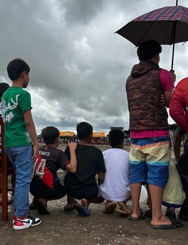 Young boys watching a local outdoor community event under a cloudy sky.