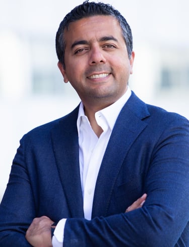 Professional portrait of a smiling businessman in a blue blazer and white shirt with arms crossed.