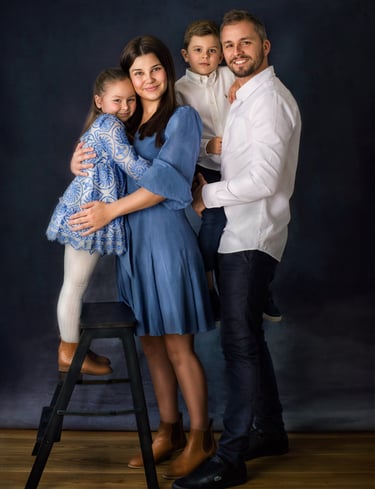 a family of four posing in a studio for a family portrait, all wearing blue and white