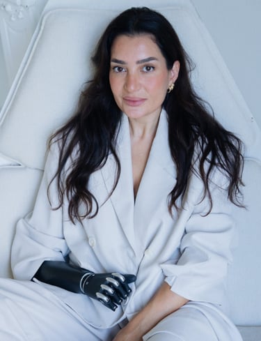 A woman in a white blazer sitting on a white chair with a bionic prosthetic arm.