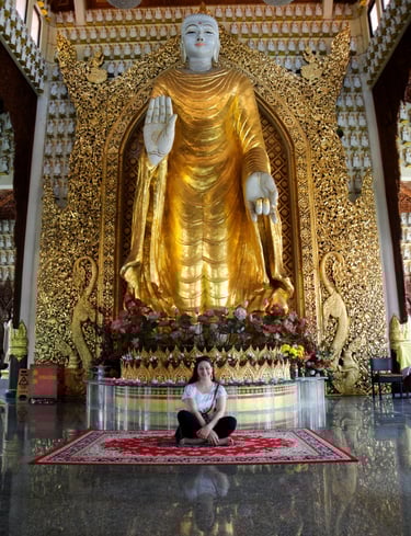 foto da autora sentada no templo abaixo das mãos de buda em penang malasia