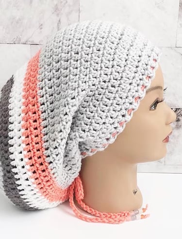 Woman wearing a large Rasta tam, locsock in light gray with orange, white, and medium gray stripes. 