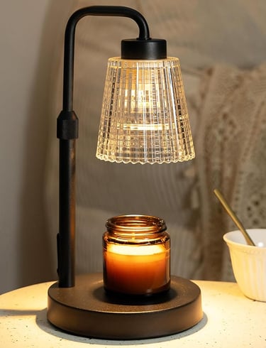 Black electric candle warmer lamp with amber jar candle and ribbed glass shade on a cozy bedside tab