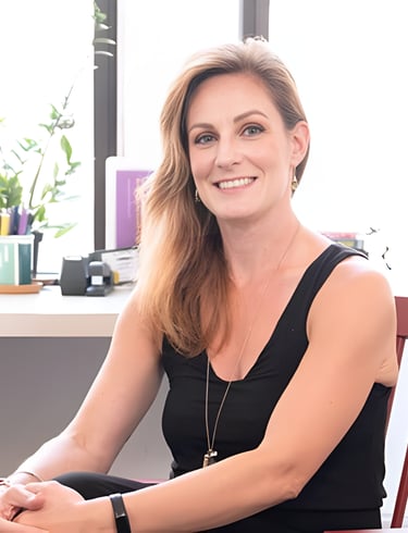 Smiling female professional in a black sleeveless top sitting in a bright modern office.