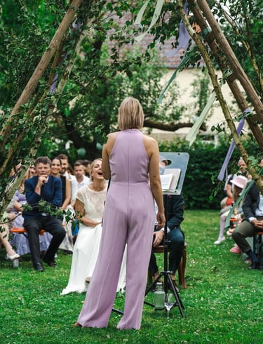 Traurednerin Silke leitet eine freie Trauung im Freien vor einem Hochzeitspaar und den versammelten Gästen.