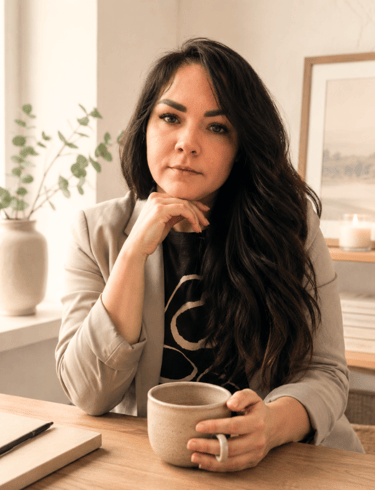 Professional woman in a blazer sitting at a desk with a coffee mug and notebook.