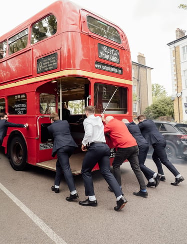 men pushing red bus Just married up the hill