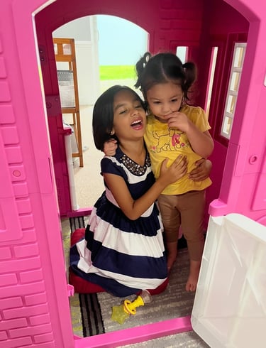 Two little girls playing in a pink toy house
