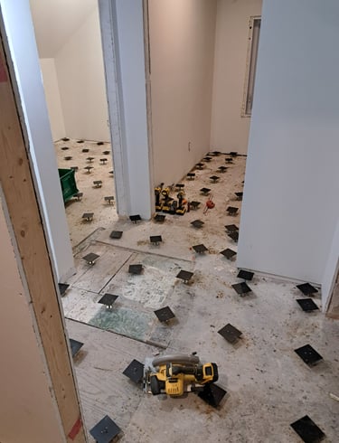 In-progress subfloor leveling installation using adjustable pedestal system during interior renovation