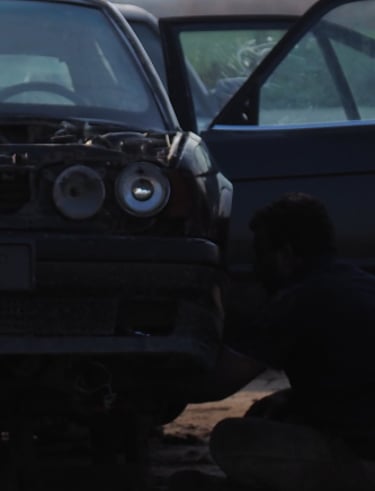 a group of Arab men in traditional clothes overlooking the dismantling of an old BMW