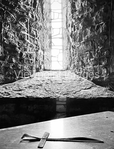Black and white photo of a small stone cross on an altar inside a medieval castle window.