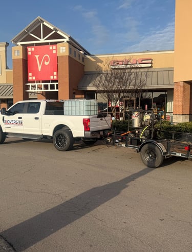 White commercial pressure washing truck and trailer parked at a retail shopping center.
