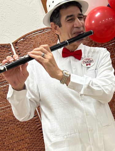 Maestro Bobby Ramirez in a white suit and red bow tie playing flute