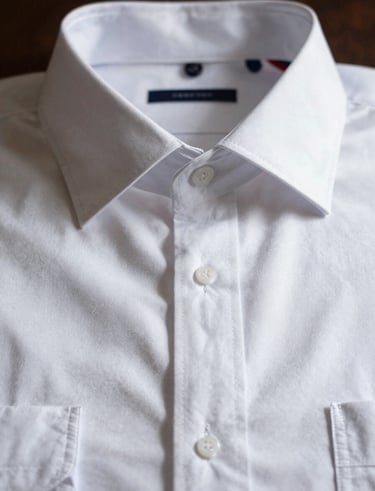 Close-up of a crisp white premium cotton dress shirt, perfectly ironed collar, soft dramatic shadow casting over the structured placket.