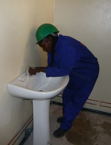 Plombière de Yaoundé portant un casque de sécurité installant un lavabo sur colonne en céramique
