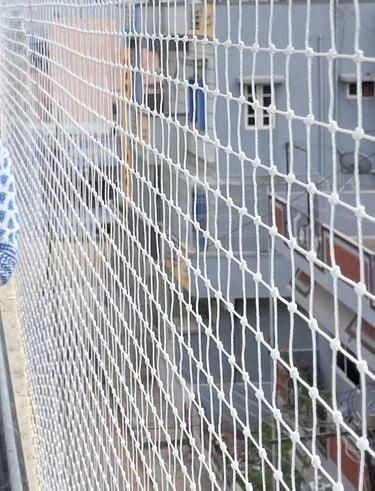 Wide shot of a balcony fully secured with pigeon safety nets overlooking a busy Mumbai street.