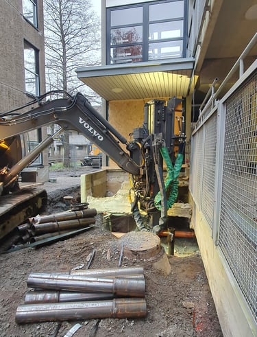 A Volvo excavator with a hydraulic pile driver attachment installs steel foundations at a construction site.