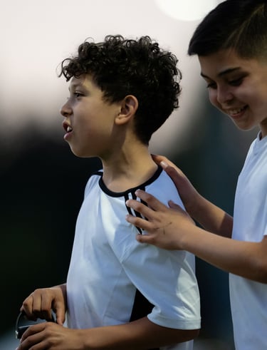 One boy watching an unseen soccer ball go wide and a second boy patting him on the back.