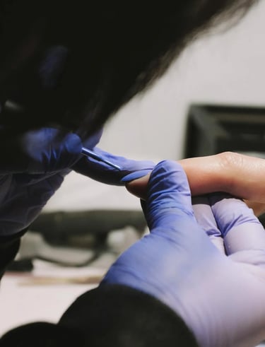 A nail tech in gloves is painting a customer's nails.