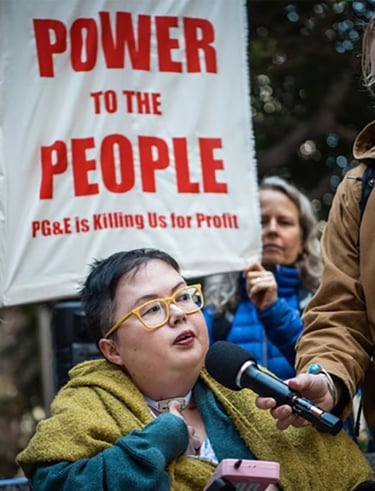 Photo of Stacey at a protest with sign that reads "power to the people PG&E is killing us for profit"