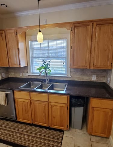 Modern kitchen with oak wood cabinets, dark granite countertops, and a triple-basin stainless steel sink.