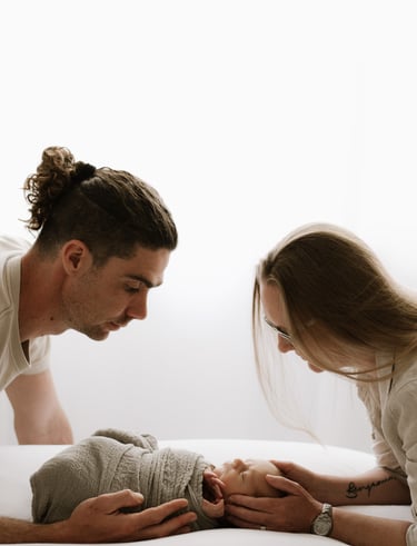 newborn photographed with his mom & dad looking down in front of a window in Adelaide Hills