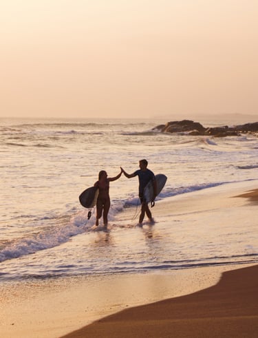 two surfers high five by the ocean