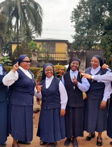 Six smiling Catholic nuns in blue and white habits posing outdoors together for a group photo.