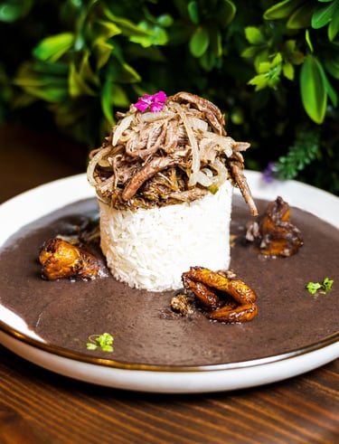 Gourmet Cuban Ropa Vieja served over white rice with black bean soup and fried plantains.