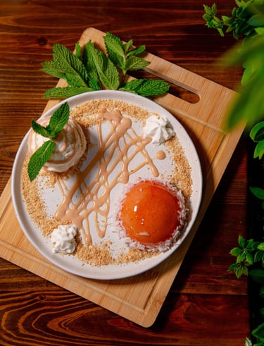 Gourmet peach dessert with fresh mint, cream, and crumble on a rustic wooden board.