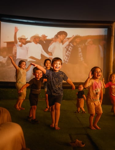 مجموعة من الأطفال الفرحين يلعبون ويرقصون أمام شاشة كبءرة في الهواء الطلق