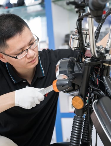Professional mechanic wearing gloves and glasses repairing a motorcycle headlight in a shop.