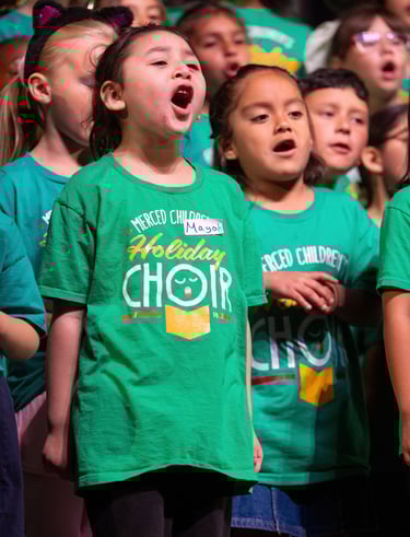Diverse group of children in green holiday choir t-shirts singing together during a musical performance.