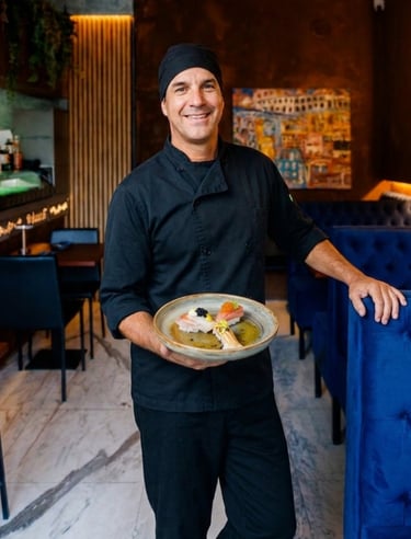 Chef Jairo Cavalcante sorri, segurando um prato de sushi autoral no interior do restaurante Okone Sushi Nikkei Porto