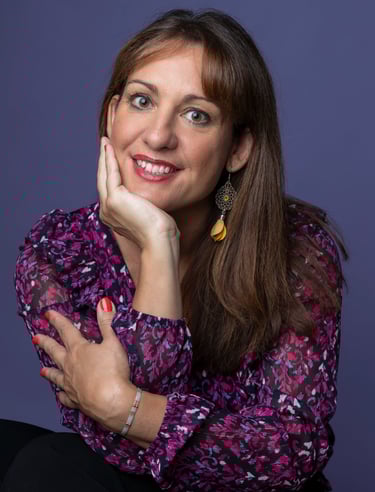 Caroline Thibault Astrothe, astrologue grande, brune, souriante avec un chemisier à fleurs violet 