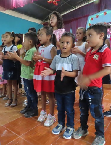 A group of children stand together clapping and singing.