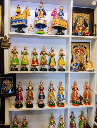 Colorful Thanjavur dolls alongside framed Thanjavur paintings for sale in Tamil Nadu
