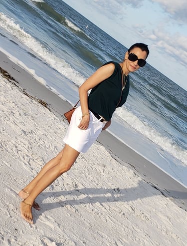 a woman in white shorts and sunglasses on a beach