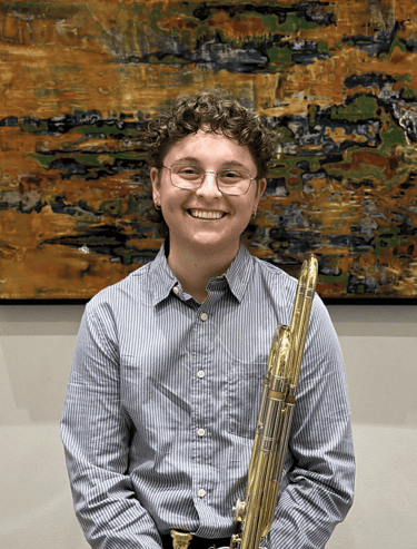 Natalie DiMundo in a blue shirt and glasses holding her trombone