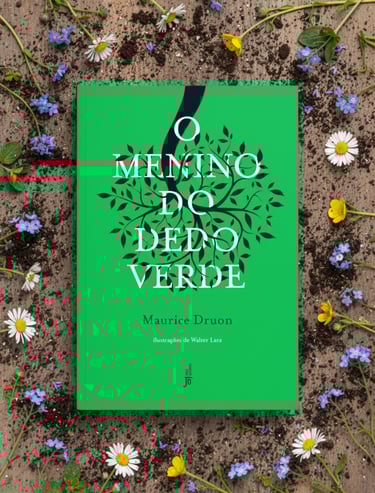 Green cover of O Menino do Dedo Verde book by Maurice Druon surrounded by fresh daisies and soil.