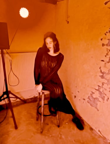 tsita zee dreamily sitting on wooden stool next to loudspeaker, warm and diffuse orange lighting.