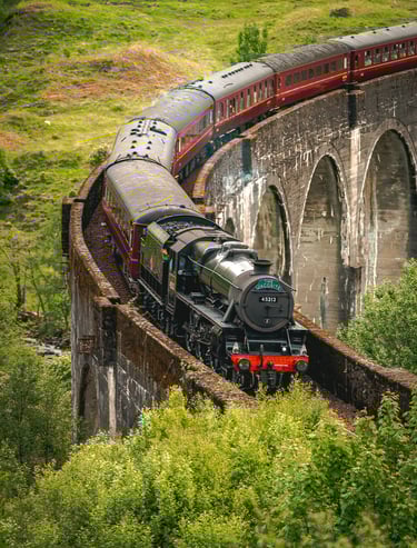 Le train Poudlard Express traverse majestueusement le viaduc de Glenfinnan, entouré de verdure luxuriante.