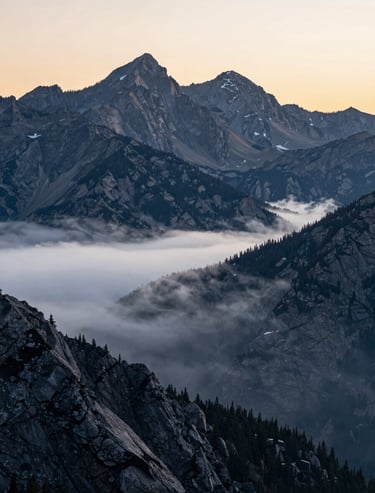 A majestic landscape of the North American / US Rocky Mountains at sunrise, captured with a telephoto lens, light silver mist and charcoal gray peaks.